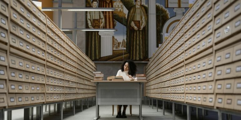 Librarian consults books in a library card aisle.